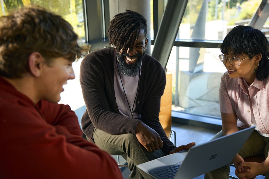 Two college students and a dean are sitting together and laughing. The dean is holding a laptop.