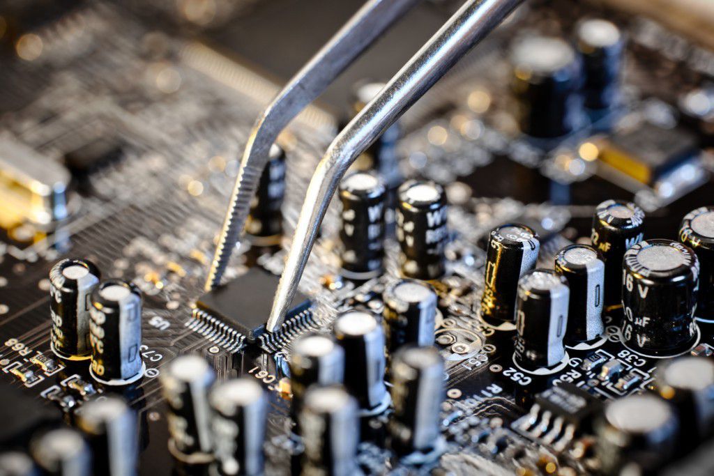 Close-up of tweezers grabbing a chip on a circuit board
