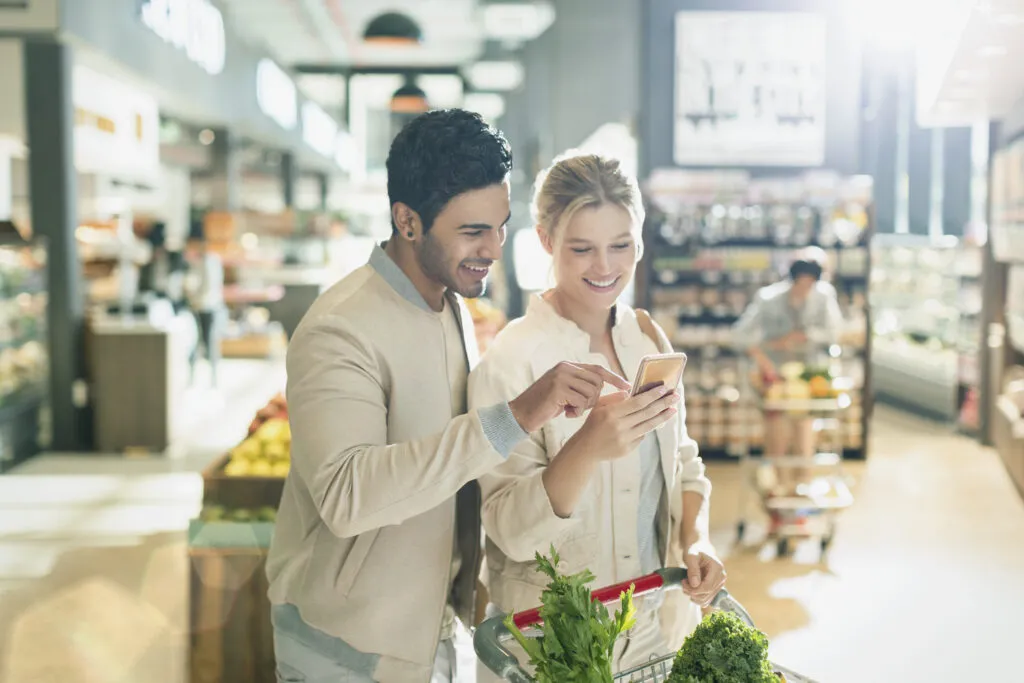 Two people shopping together and using cell phone in grocery store market