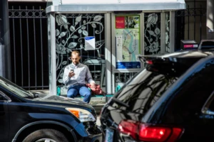 person sitting at a bus stop, looking at a smartphone