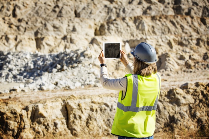 Rear view of female architect in protective workwear photographing quarry through digital tablet