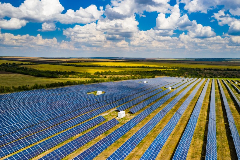 An expansive solar array stretches across fields, under a bright sky.