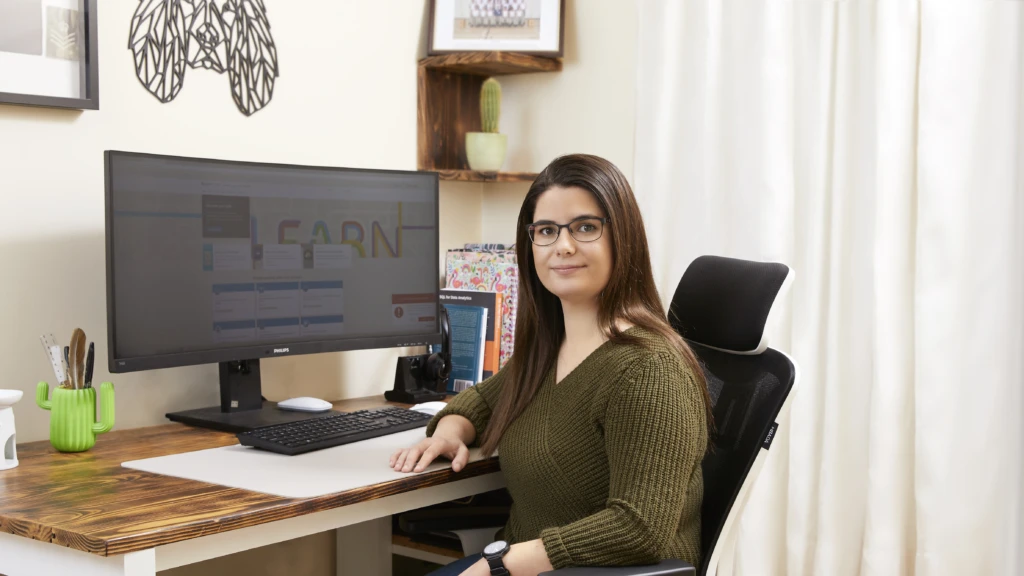 Amelia sits at her desk, smiling at the camera. On the computer monitor is Microsoft Learn