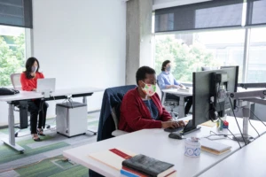 Male and female employees wearing face masks and working at their socially distanced desks.