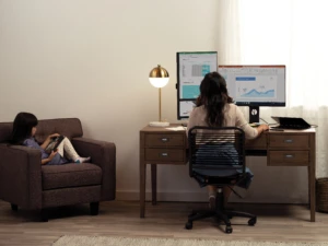 Woman working from home on data strategy with her child working on remote learning next to her
