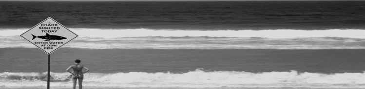 A black and white photo of a beach and a warning sign