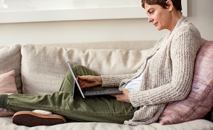 A woman sits on her couch with an open laptop.
