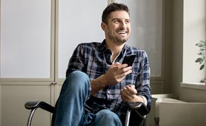 A man sits back in his chair, smiling and holding a smartphone.