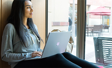 Image of a worker smiling out a window with her laptop open.