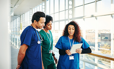 Image of three doctors in scrubs looking at digital tablet and discussing