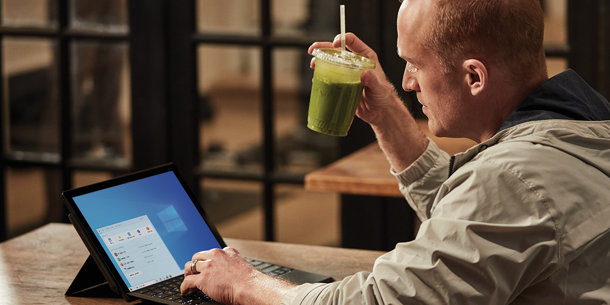 An IT worker holding a smoothie and working on his laptop.