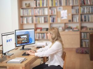 Woman sitting at computer with two monitors, typing on a keyboard