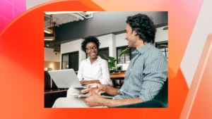 Two people smiling at each other, working together in an office, with an orange and pink graphic background