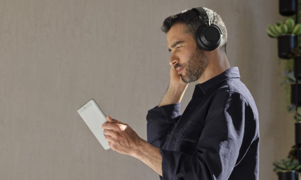 Adult male holding a platinum Surface Go 4 (Go 3) in tablet mode while wearing Surface Headphones 2+.