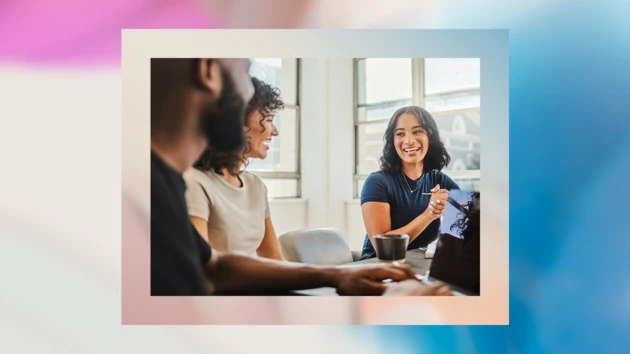 A diverse group of coworkers collaborate in an office space while one takes notes on his laptop.