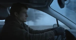 A still-frame from the Microsoft Copilot Game Day Commercial: a man wearing a coat and gloves driving a car in the winter with snow in the background.