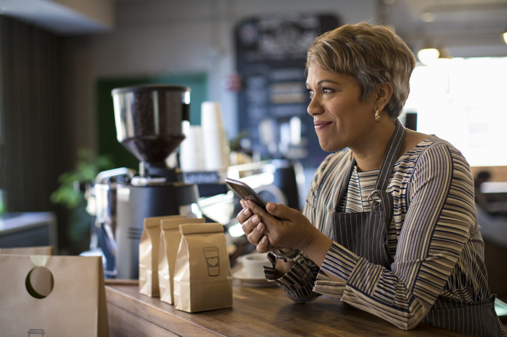 Frontline worker achieving in retail work space using phone. Mobile inventory. Coffeshop owner. Small Business.