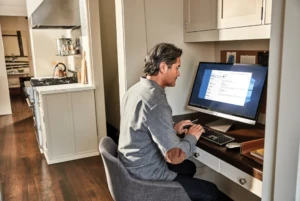 Man sitting at computer near kitchen.