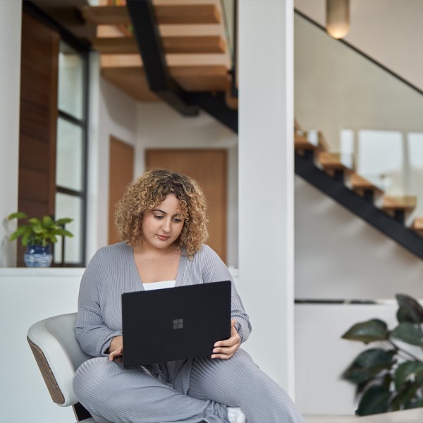 A person sitting on a chair, holding a laptop, working from home.