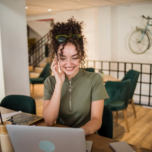 Woman talks on the phone while working on a laptop in a cafe.