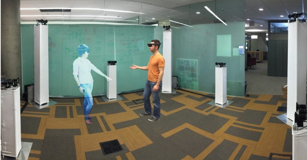 A man wearing a Hololens device standing in front of a 'hologram' woman 