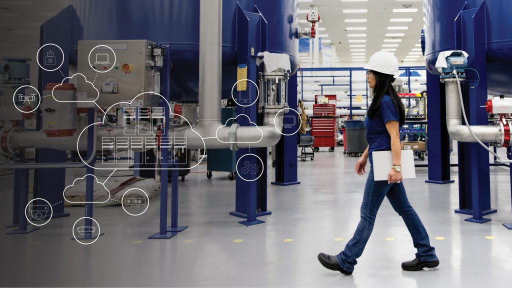woman wearing a hardhat walking across a factory floor with an overlay of cloud, server and edge-computing icons
