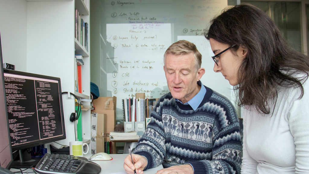Simon Peyton Jones writing with a fellow researcher at a desk