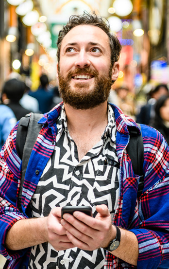 Male tourist in patterned shirt holding a cellphone looking up on busy street