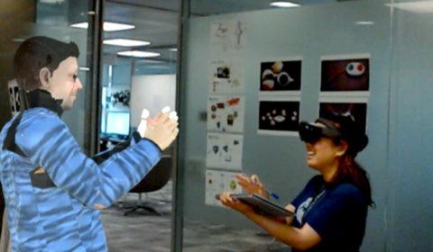 Senior Researcher Sean Rintel, using VROOM, interacts with Research Assistant Priscilla Wong, who is wearing a HoloLens. Sean’s photorealistic avatar is clapping along with Priscilla.