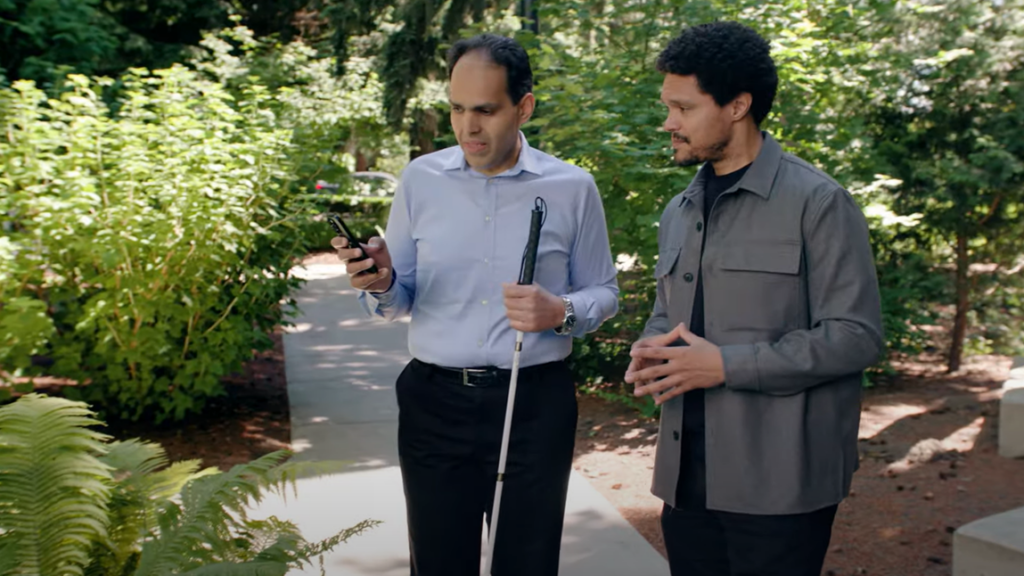 Blind person showing someone the Seeing AI App on phone outside in a wooded setting.