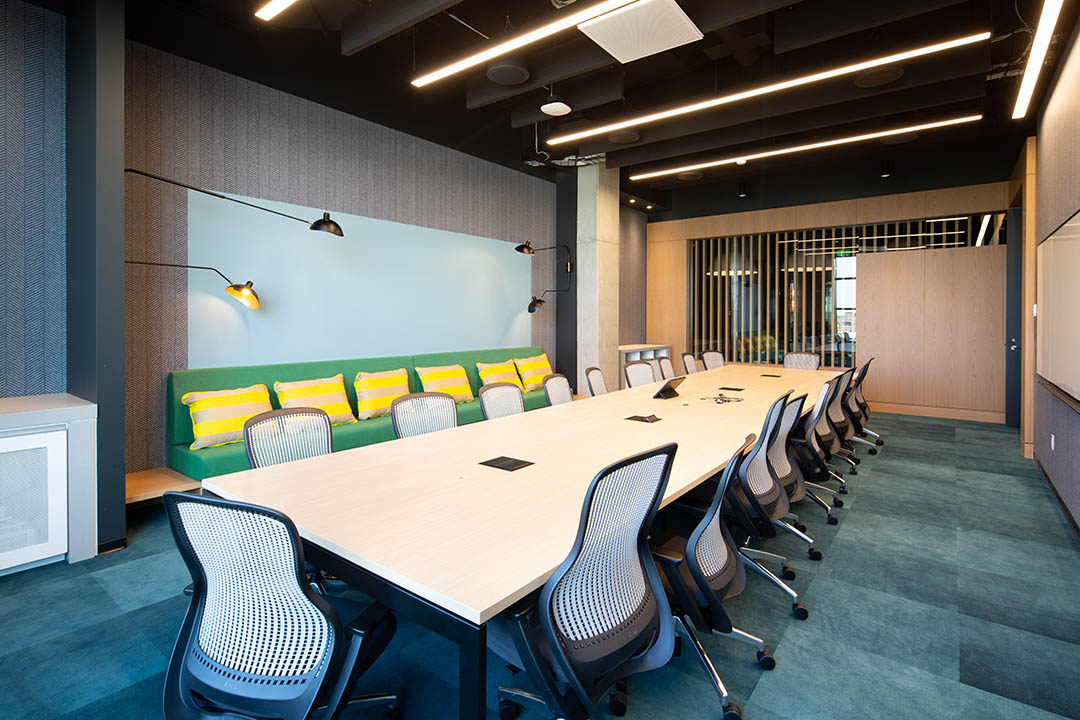 A large office space with a long table and chairs, bench seating, and whiteboard at Microsoft Research Montreal. Un grand espace de bureau avec une longue table et des chaises, des sièges de banc et un tableau blanc chez Microsoft Research Montréal.