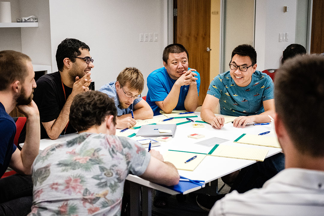 Microsoft Research Montreal researchers and interns collaborating around a table. Des chercheurs et des stagiaires de Microsoft Research Montréal collaborent autour d’une table.