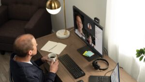 A man sits at a computer having a remote meeting while drinking coffee