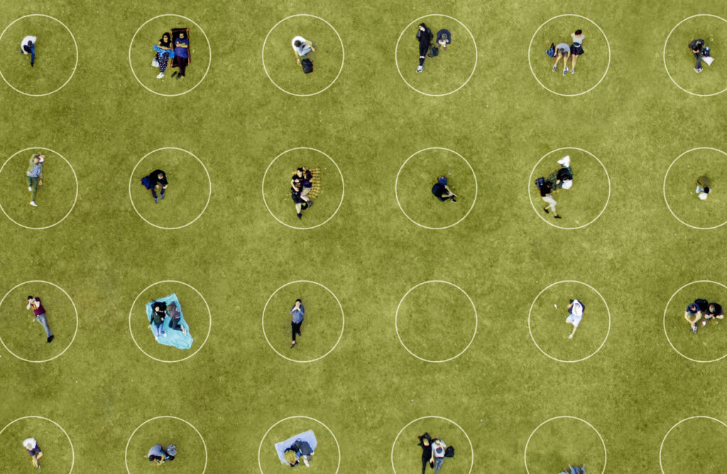 Birds-eye view of a park lawn with people sitting in circles.