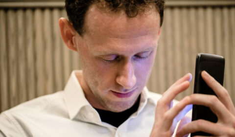 A close-up of a man wearing casual clothing, he has his smartphone in his hand and he is using an assistive mobile app for people with vision disabilities to assist him.