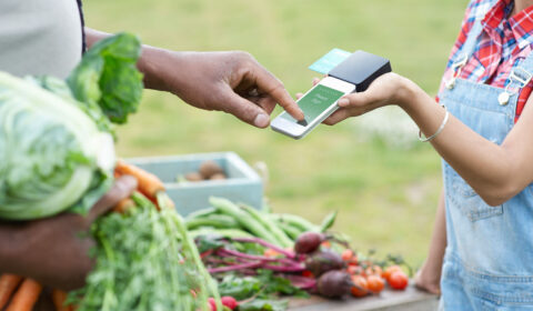 Urban innovation: farmer selling vegetables to a customer using a cellphone to pay