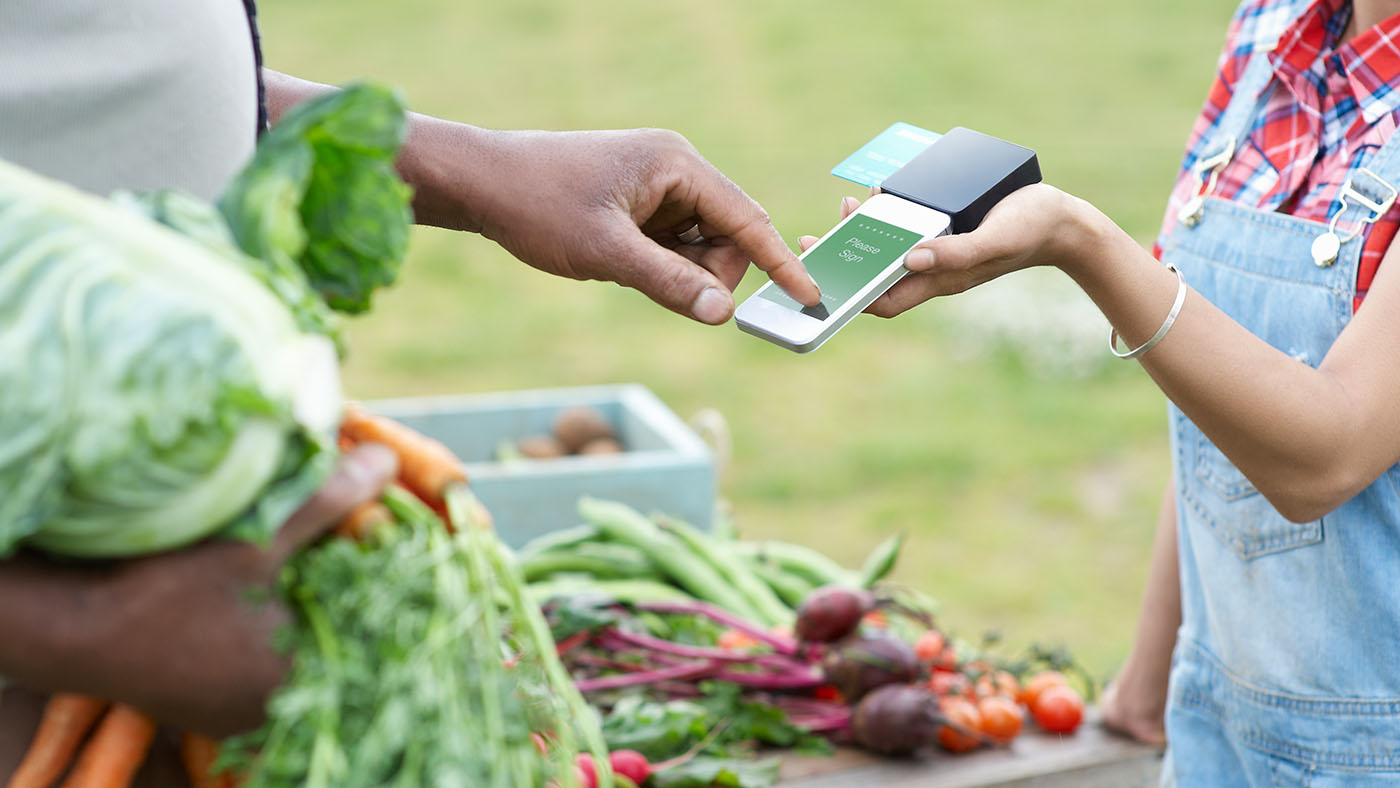 Urban innovation: farmer selling vegetables to a customer using a cellphone to pay
