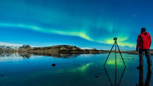 Climate Research Initiative - photo of a man with a tripod looking up at the Northern Lights