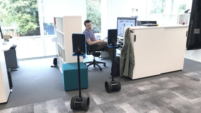 A man talks to people in two telepresence robots in an office