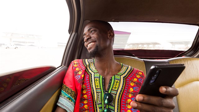 Young African man in a car holding a mobile phone and laughing
