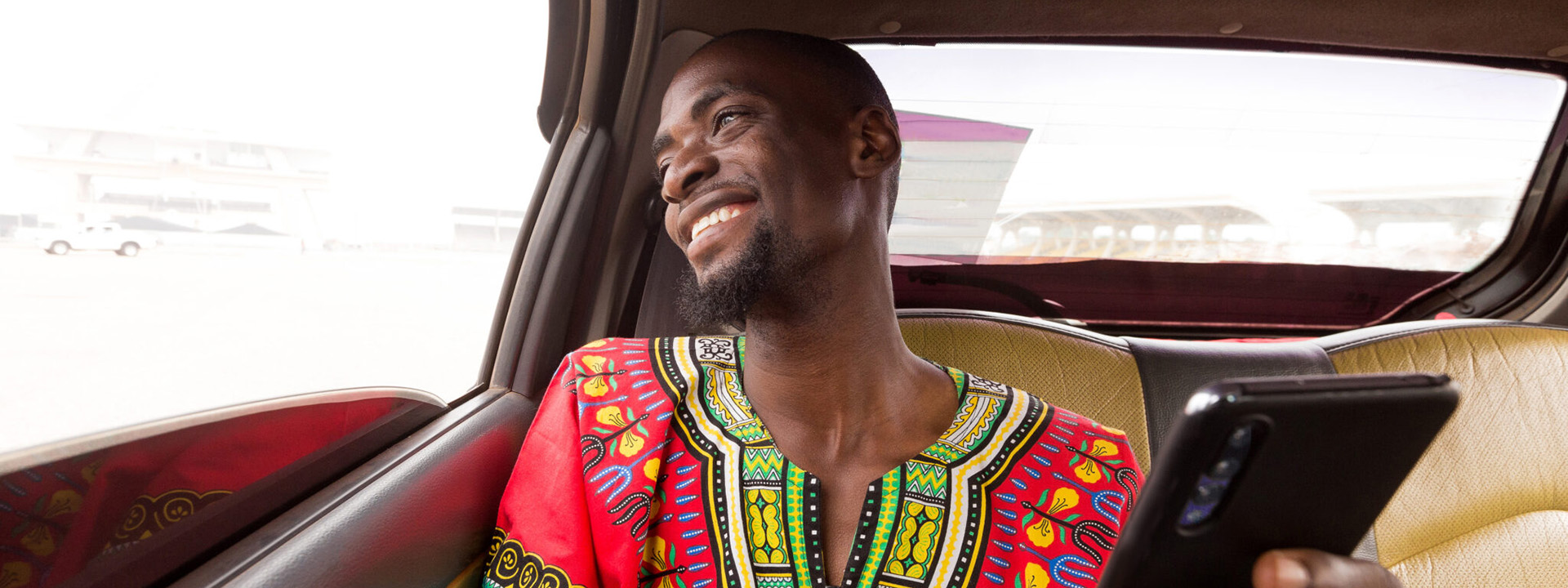 Young African man in a car holding a mobile phone and laughing