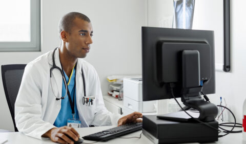 Male Doctor Using Computer At Desk In Hospital