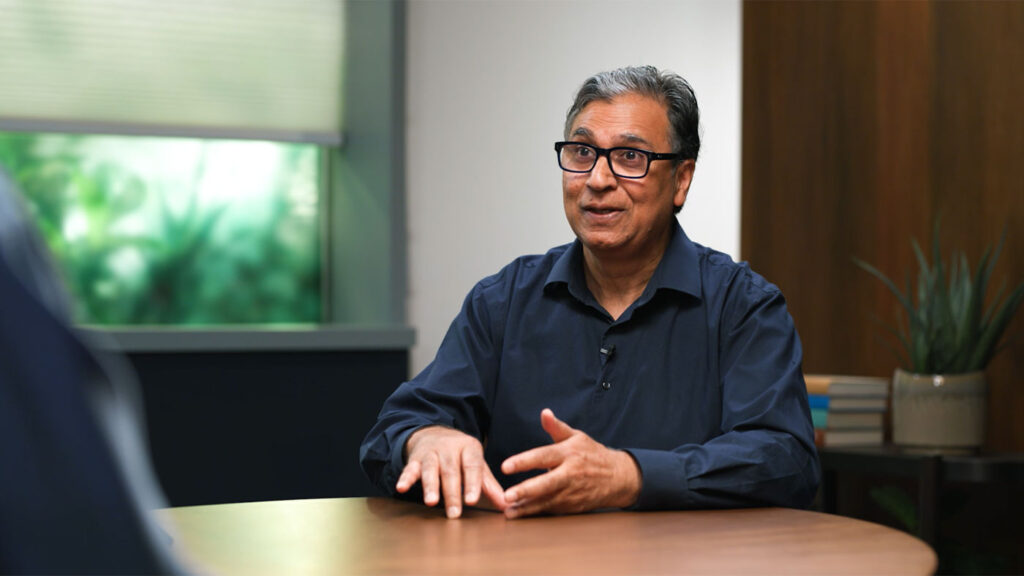 Vijay Mital sitting at a table having a discussion with Peter Lee and Gretchen Huizinga