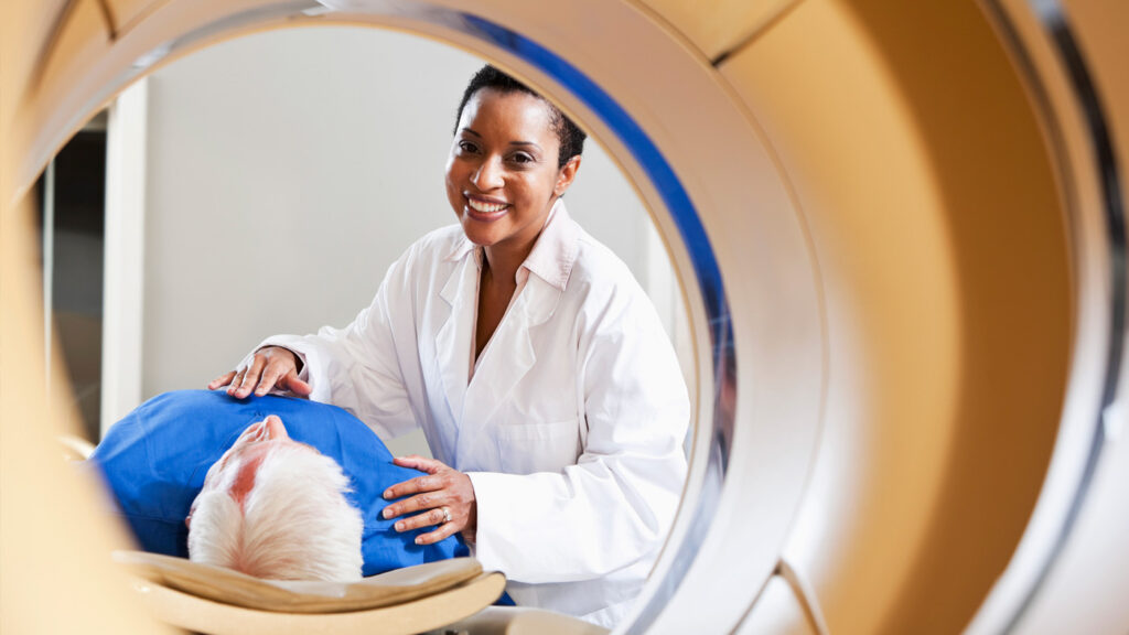 AI4Good - Expand Opportunity | photo of a medical tech standing next to a patient going into an MRI machine