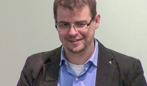 a man wearing a suit and tie smiling and looking at the camera