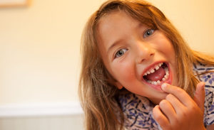 Image of a girl pointing to a missing tooth and smiling.