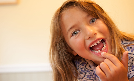 Image of a girl pointing to a missing tooth and smiling.