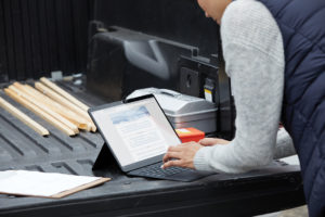 Adult female standing at the back of a pickup truck using a black Microsoft Surface Pro X in laptop mode with Microsoft Edge screen shown.