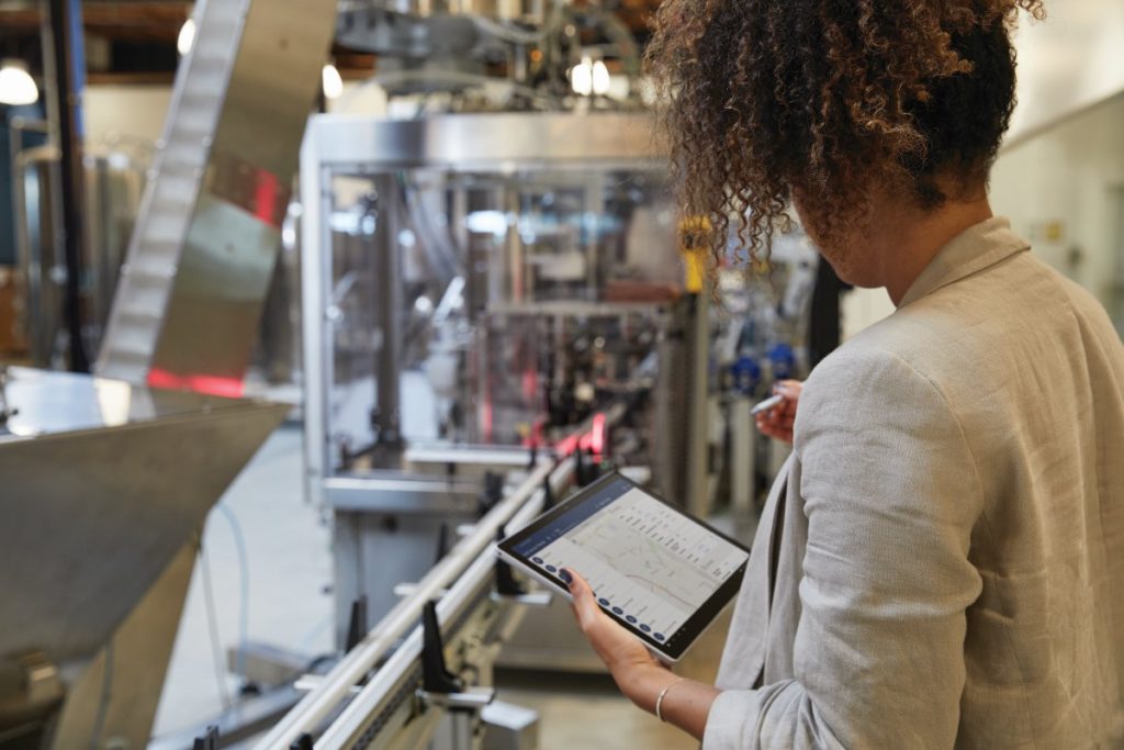 Adult female in an industrial factory setting holding a platinum Microsoft Surface Pro 7 in tablet mode while preparing to use a Microsoft Surface Pen with Microsoft Dynamics screen shown.