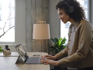 Adult female wearing Surface Headphones 2+ standing at a desk, working on a Surface Pro X in Microsoft Outlook.